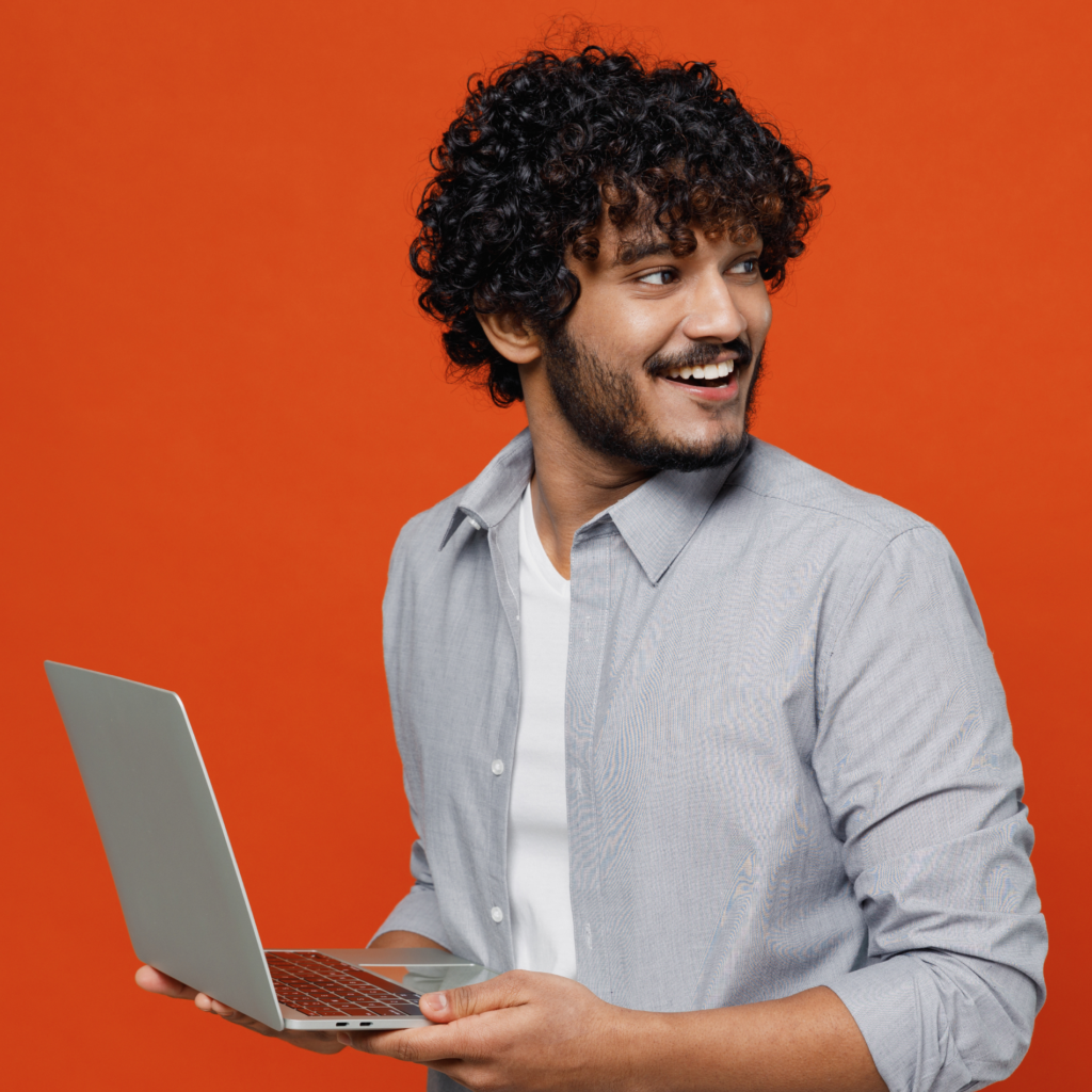 A smiling man holding a laptop and looking to the side, against an orange background, conveying a positive and engaged attitude